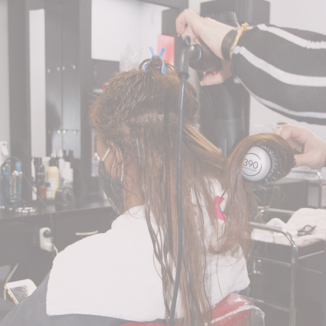 Hair stylist blow-drying and styling a brown skinned woman hair; woman with sew in weave.